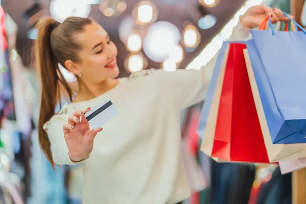 La chica tiene una tarjeta de crédito y bolsas de compras con una tienda . — Foto de Stock