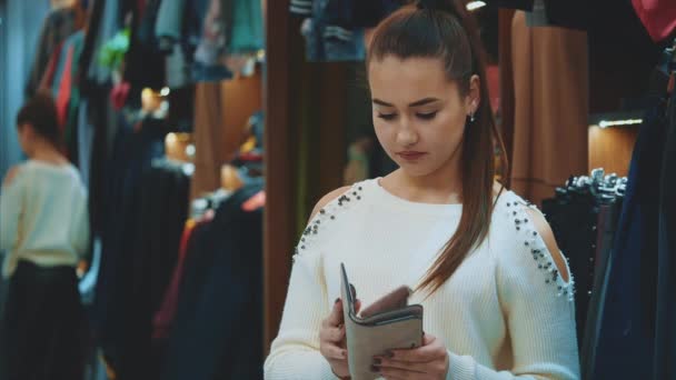 Молодая девушка в магазине ищет кредитку в бумажнике, чтобы заплатить за вещи. . — стоковое видео