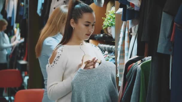 Una hermosa dama en una tienda de ropa elige un armario adecuado para ella . — Vídeo de stock