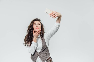 Beyaz bir arka plan üzerinde güzel kıvırcık saçlı Genç iş kadını. Bu sırada kendini bir sephi yapıyor telefonunda resimlerini alıyor