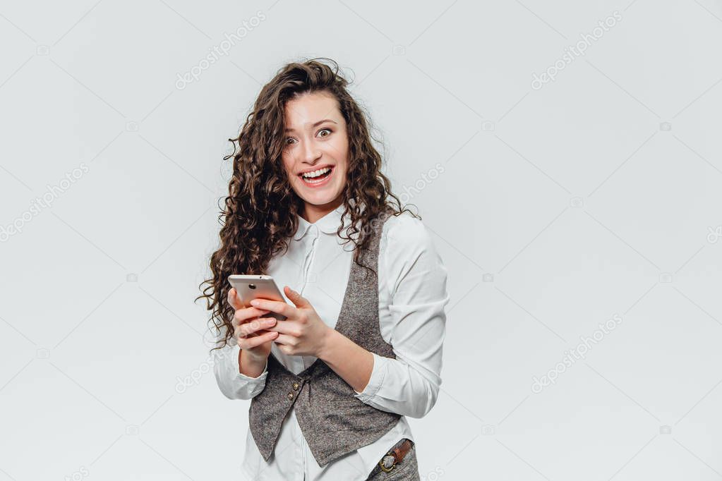 Young business lady with beautiful curly hair on a white background. During this time, he emotionally views his photos on the phone