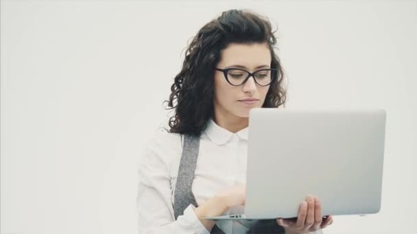 戴眼镜的精力充沛的年轻女孩站在白色的背景上 在此过程中 笔记本电脑在查看文档和新插座时手持 — 图库视频影像