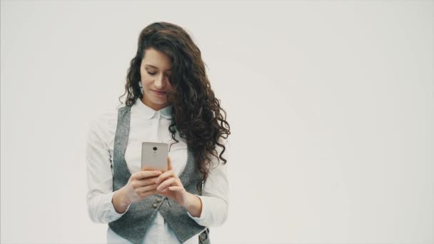 Μια ενεργητική κοπέλα με τα σγουρά μαλλιά είναι φωτογραφήθηκε στο τηλέφωνο. Έχοντας κάνει μια sephi. Σε λευκό φόντο. — Αρχείο Βίντεο