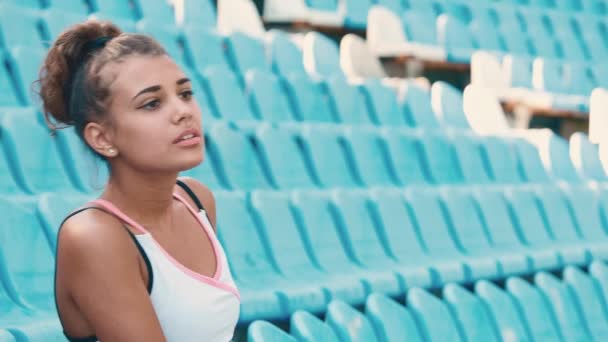 Boční pohled na krásná mladá žena sedící na tribuny na sportovní stadion. — Stock video