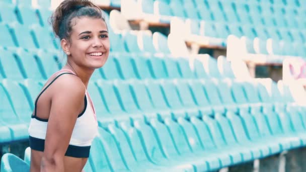 Vista lateral de la hermosa joven sentada en tribunas en el estadio deportivo . — Vídeos de Stock