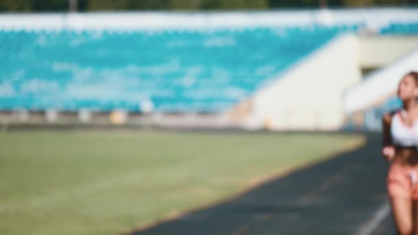 Retrato de una chica fuerte en ropa deportiva corriendo en el estadio. Hermosa chica corre en el estadio y escucha al jugador . — Vídeo de stock