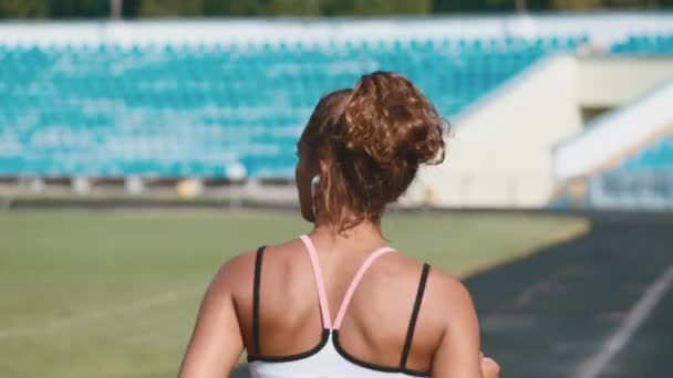 Portrait d'une fille forte en tenue de sport courant dans le stade. Belle fille court dans le stade et écoute le joueur . — Video