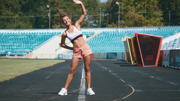 Sport, oefeningen buiten. Meisje doet die zich uitstrekt over stadion. Opzij buigen. — Stockvideo