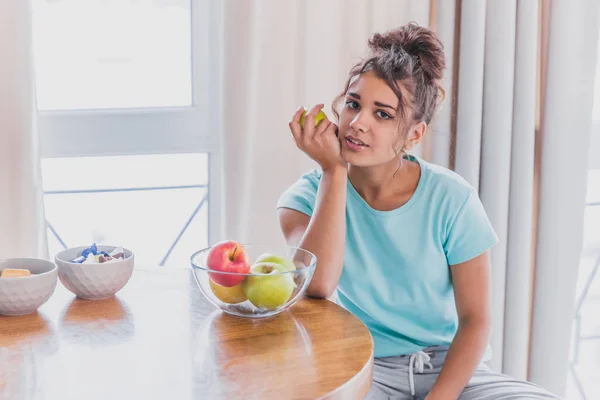 Молодая счастливая женщина освежает с чашкой кофе, закуски и свежие фрукты на кухонном столе рано утром . — стоковое фото