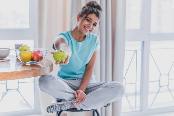 Молодая счастливая женщина освежает с чашкой кофе, закуски и свежие фрукты на кухонном столе рано утром . — стоковое фото