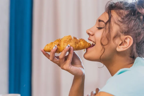 Foto de una joven alegre feliz. Ir a la mesa y comer croissant . —  Fotos de Stock