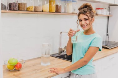 Mutlu güzel genç kadın içme suyu. Beyaz kadın modeli şeffaf cam elinde tutan gülümseyerek.