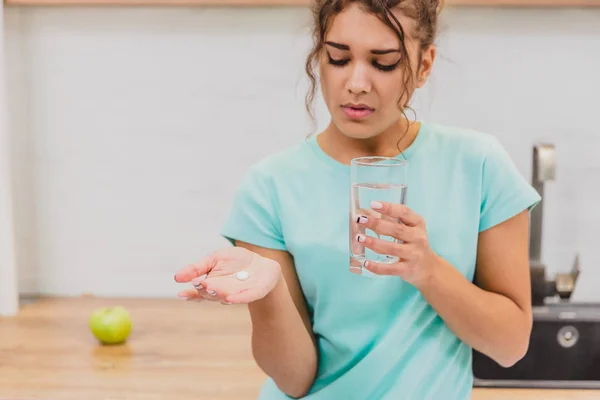 Woman holding pill and glass of water in hands taking emergency medicine, supplements or antibiotic antidepressant painkiller medication to relieve pain.