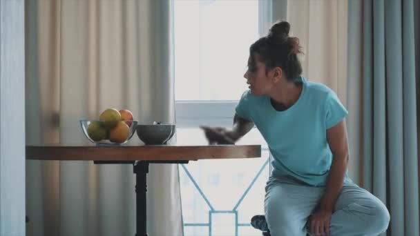 Eine junge glückliche Frau erfrischt sich am frühen Morgen mit einer Tasse Kaffee, Snacks und frischem Obst auf dem Küchentisch. — Stockvideo