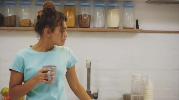 Underbara, vackra, unga kvinna håller glaset rent vatten och ler medan stående i köket på morgonen — Stockvideo