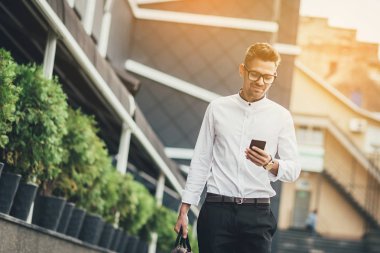 Kendine güvenen genç işadamı şehirde cep telefonu kullanarak. Güneş arka plan