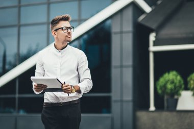 Kendine güvenen genç işadamı finansal belgeler elinde tutan ve Ofis Binası yakınındaki kentsel ortamda gezinme şık kurumsal takım elbise giymiş