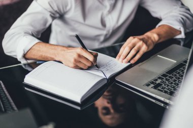 adam dizüstü bilgisayar, çalışma masasına oturur ve notlar not defterinde yapar. Online pazarlama, eğitim, e-öğrenme. yakın çekim