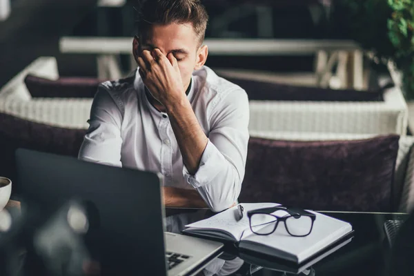 Handsome businessman getiing tired of work on laptop at the cafe. Attractive bearded guy rubbing his eyes and forehead — Stock Photo, Image