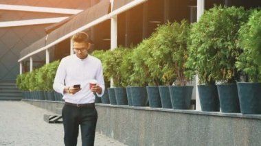 İş elbiseleri ve gözlük giymiş genç iş adamı işe gidiyor. Bu süre boyunca, kahve elinde, seyir telefon güneş sızıntı ile tutarak.