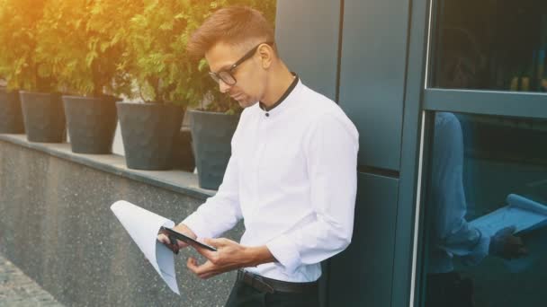 A young businessman dressed in business clothes and glasses stands at the office. — Stock Video