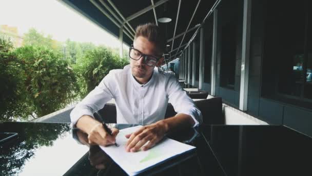 Joven hombre de negocios vestido con ropa de negocios y gafas sentado en la oficina . — Vídeo de stock