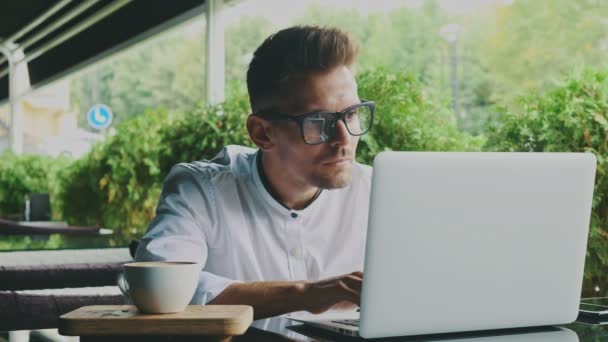 Νεαρός επιχειρηματίας ντυμένος με επαγγελματίες και τα γυαλιά, κάθεται σε μια καφετέρια. — Αρχείο Βίντεο