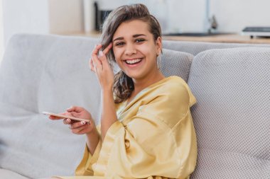 Genç bir kız seyir telefon süre yakından göründüğünü izliyor ve kanepede oturan bir sabahlık giymiş. Sabah.