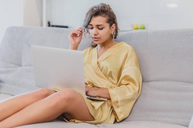 Esmer kanepede onun evinde yatarken onu laptop ile rahatlatıcı. Rahat bir kanepede rahatlatıcı ve evde bir dizüstü bilgisayar kullanarak mutlu genç kadın.