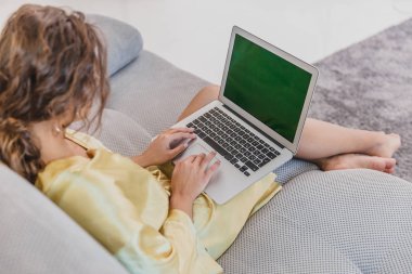 Gülümseyen genç kadın evde rahat bir koltukta rahatlatır gibi bir dizüstü bilgisayar kullanarak. Bir çekici eğlenceli model tipik bir bilgisayar ile.