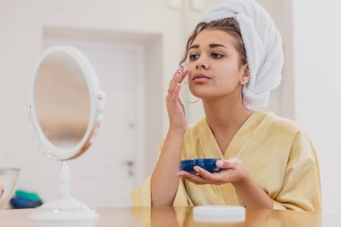 Sevimli kız onun güne başlamak hazırlanıyor. Yüzünde bir nemlendirici kullanır. Bu sırada o kafasında bir havlu var.