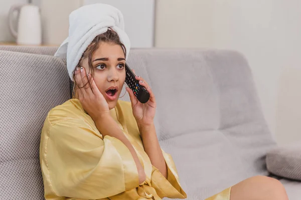 A happy woman with a remote control, choosing a television channel raises the remote control to the ears of talking. During the rest after the bath.