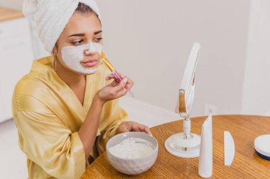 Evde Genç bir kız bir fırçayla yüzünde bir maske koyar. Bu süre içinde o aynaya bakar.