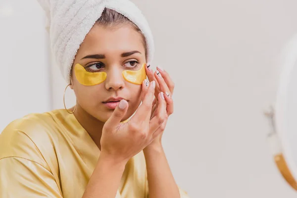 Sebuah potret closeup dari seorang wanita cantik setelah mandi dengan handuk di kepala menempatkan patch di bawah mata dari keriput dan lingkaran gelap . — Stok Foto
