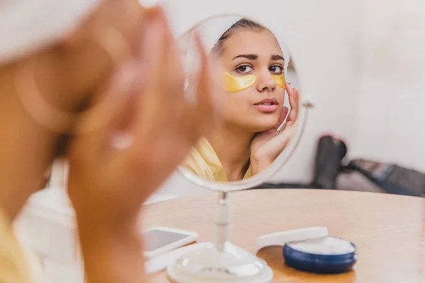 Un retrato de cerca de una hermosa mujer después de un baño con una toalla en la cabeza pone parches debajo de los ojos de las arrugas y las ojeras . — Foto de Stock