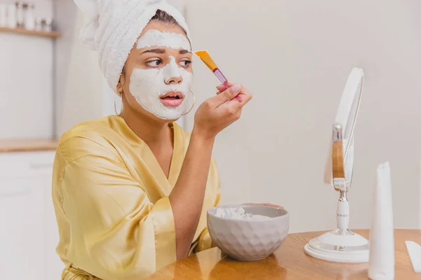 Face and body skin care, face treatment at home concept. Happy young woman applying a white mask on her face with a brush. — Stock Photo, Image