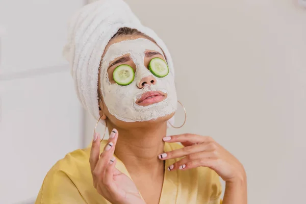 Seorang wanita muda yang cantik mendapat masker wajah di pusat spa, berbaring dengan mentimun di matanya. Bahagia dan mendapat banyak kesenangan . — Stok Foto