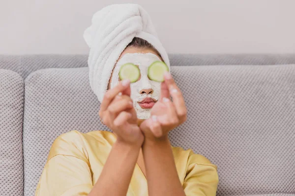 Hermosa joven haciendo tratamientos de spa en casa, acostada con pepinos en los ojos. Feliz y sonriente . — Foto de Stock