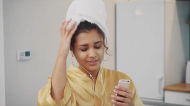 Genç kadın gülümsüyor. Uyanma spa sabah sahiptir. Mutlu kız başında bir havlu ile yatak odasında yüzünde bir maske. İyi cilt tonunu