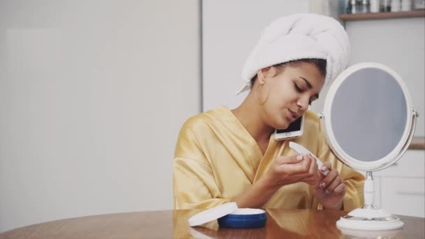 La jeune femme sourit. Se réveiller le matin Fille heureuse avec une serviette sur la tête dans la chambre. Bonne couleur de peau. Serre les limes à ongles et parle par téléphone . — Video