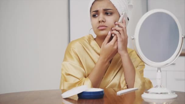 Uma jovem acorda de manhã. Menina feliz com uma toalha na cabeça no quarto. Bom tom de pele. Senta-se e fala por telefone . — Vídeo de Stock