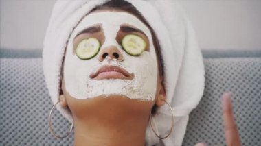 Güzel bir genç kadın bir yüz maskesi ile salatalık gözlerinde yalan spa Center'da alır. Mutlu ve eğlenceli bir sürü alır.