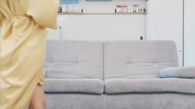 Genç kadın kanepede de odada bir bornoz Sit. O içecekler kahve kanepede oturan ve Tv izlerken.