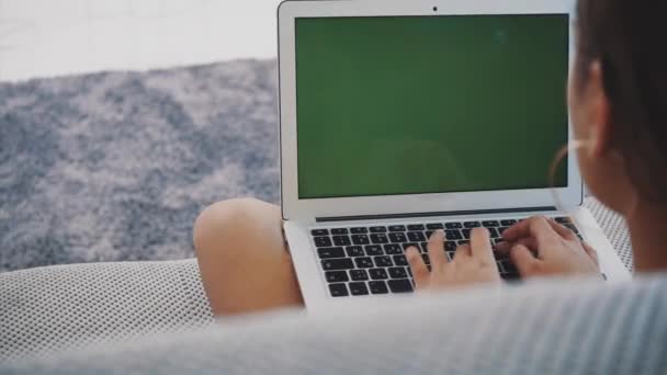 Jovem sorridente usando um laptop em casa enquanto relaxa em um sofá confortável. Um modelo divertido atraente com uma digitação de computador. Tela verde . — Vídeo de Stock