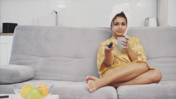 Lycklig kvinna med en fjärrkontroll, att välja en Tv-kanal under vila efter ett bad. På huvudet är en handduk. — Stockvideo