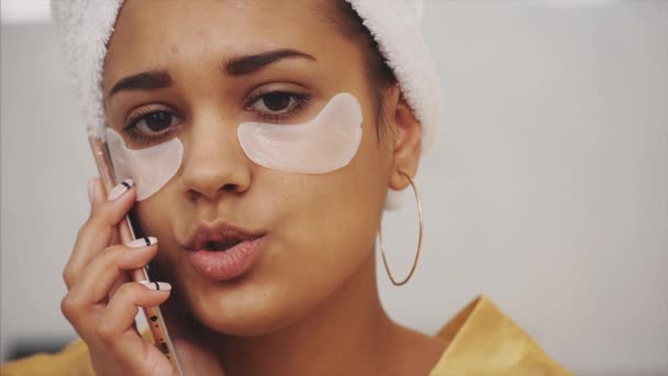 Closeup πορτρέτο του όμορφη γυναίκα μετά από μπάνιο, με πετσέτα στο κεφάλι βάζει μπαλώματα κάτω από τα μάτια από τις ρυτίδες και τους μαύρους κύκλους. — Αρχείο Βίντεο
