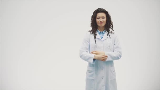 Uma jovem mulher séria em uma mulher caucasiana em um robe de laboratório olhando para você e segurando o fonendoscópio fora de controle. Retrato de uma mulher de cabelo muito escuro - um médico vestindo uniformes brancos. O — Vídeo de Stock