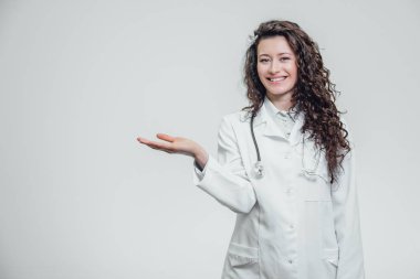Beyaz bir sabahlık bir genç kız doktor. İşaret parmağı ile geri işaret ederken. Ürün gri bir arka plan üzerinde gösterilen.