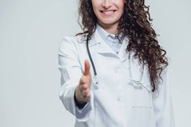 Mutlu genç gülümseyen kız doktor portresi. Beyaz bir elbise giymiş. Düz duran, bir yandan dümdüz gri arka plan önünde koyar.