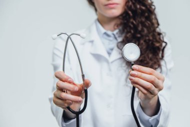 Bir el ile bir stetoskop, arka planda doktor yüzü. Yakın çekim muayene kavramı. Gri arka planı.